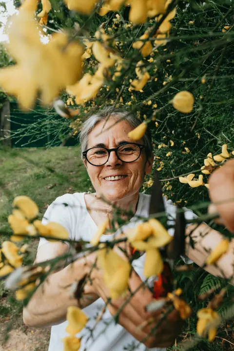 A woman smiling among flowering shrubs
