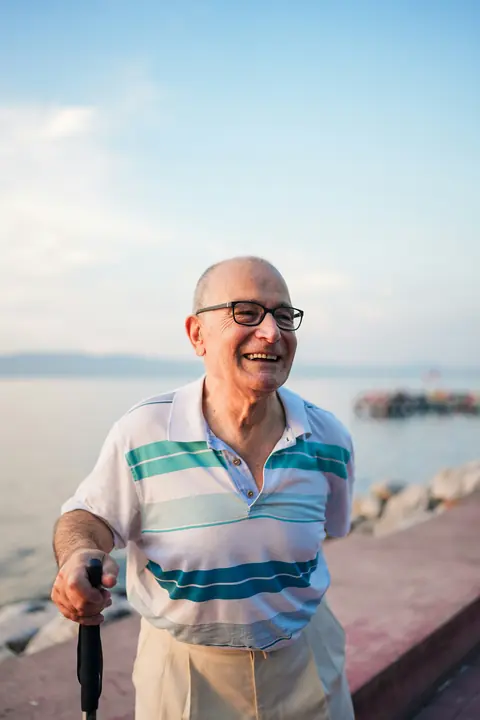 A smiling man with a walking stick by the sea