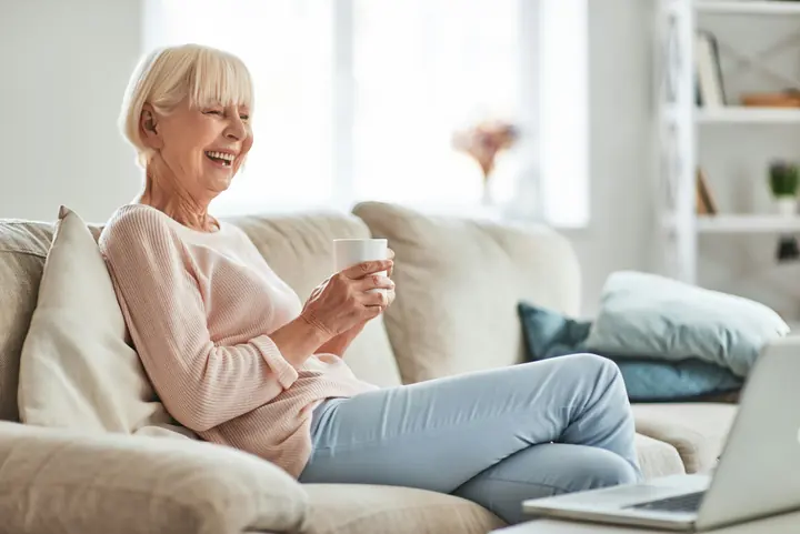 A woman laughing on her sofa with a cup of tea